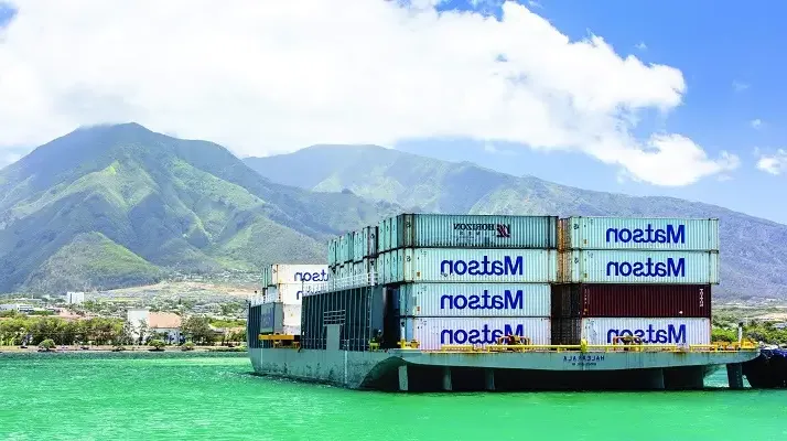 澳博体育app下载 barge Haleakala loaded with 澳博体育app下载 containers arrives in Kahului with green mountains and clouds in the background.